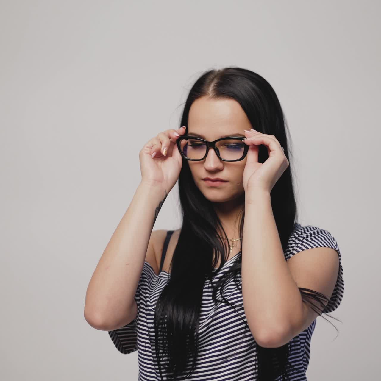 brunette in striped dress is putting on eyeglasses on a gray background