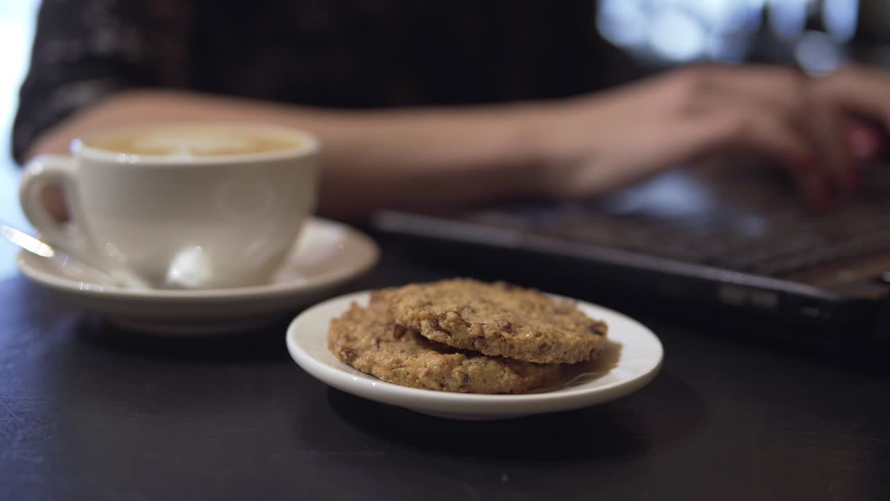taza de café y coockies. mujer trabajando con computadora portátil en el fondo