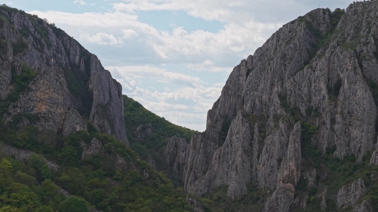 Uma vista deslumbrante de um cânion de montanha rochoso, cercado por penhascos íngremes de calcário e uma floresta verde exuberante.