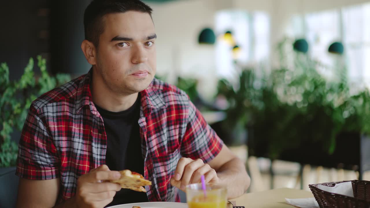 handsome man in a plaid shirt is eating pizza at a cafe for lunch on a blurred background. Pizzeria