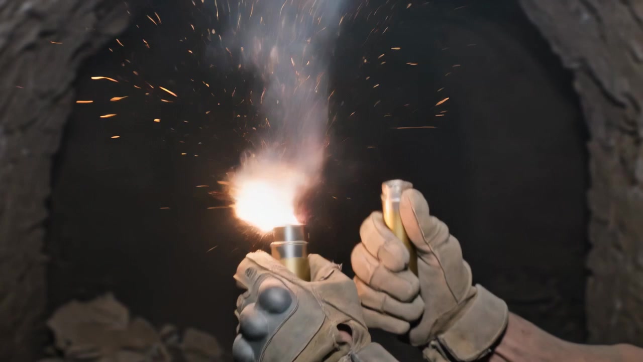 Mano con guanto tattico color sabbia che colpisce un contenitore metallico in un tunnel, illuminando le pareti di pietra.