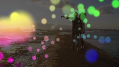 Animation-of-colorful-spots-of-light-over-african-american-couple-walking-on-the-rocks-near-the-sea