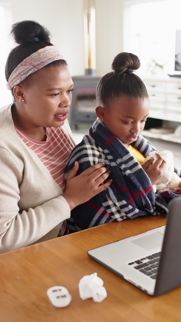 Vertical video of african american mother and daughter on laptop video call to doctor, slow motion