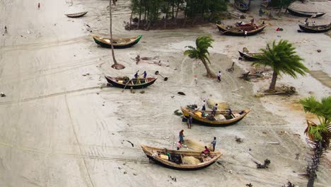 aerial view of fisherman repairing fish nets besides traditional wooden boats on kuakata sea beach, bangladesh