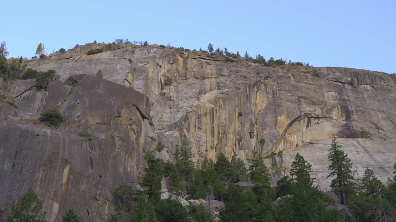 4K wide pan sweeps left-to-right across Yosemite’s towering granite escarpment, unveiling massive slabs, talus benches, and streaks of desert varnish
