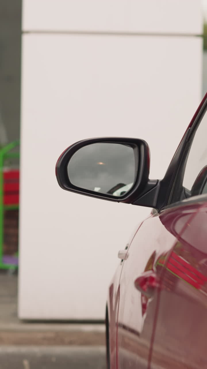 dama elegante en elegante traje verde cierra la puerta del coche rojo alejándose. espejo lateral de un vehículo moderno contra el edificio de oficinas de primer plano en cámara lenta