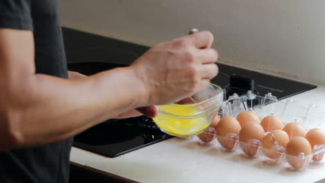 man beating eggs in a glass bowl near ceramic stove top in kitchen