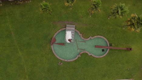 drone view of a couple standing on a bridge over a violin-shaped lake in an elegant garden.