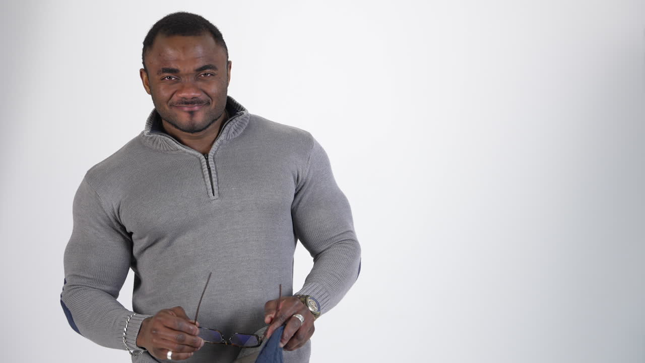 Portrait of african athlete in sweater. Black skinned guy is standing in studio and smiling. Afro american man puts on his glasses and looks on camera. Copy space.