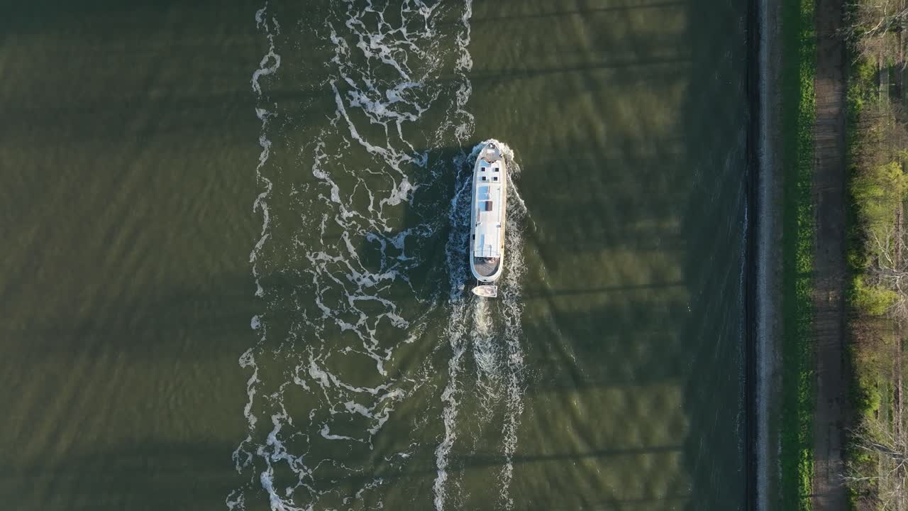 Zoom indietro zenitale dall'alto che mostra un battello passeggeri che naviga sul fiume Anversa lasciando scie d'acqua in una giornata di sole limpido