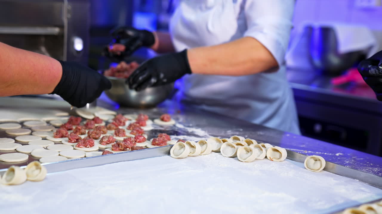 Three cooks collaborating in the kitchen producing meat ravioli. The workers spread responsibility at different stages of making pelmeni.
