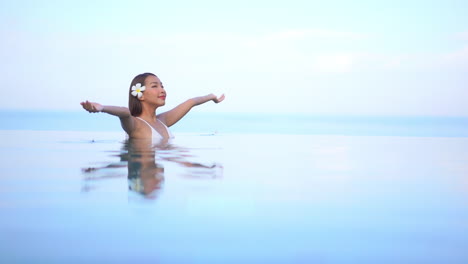 summer girl in relaxing in swimming pool spreading arms, soft focus