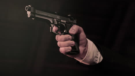 close up on man's hands in suit lifting up a pistol, dark background