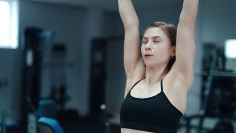 slim woman in a black top and leggings performs an exercise with her hands with dumbbells in the gym. sport equipment. blurred background