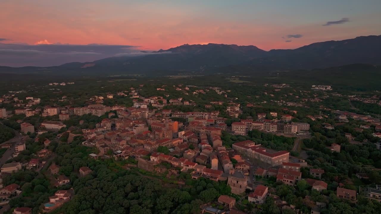 Aerial drone shot of the old town of Porto vecchio, Corsica, France at sunrise. High view of the citadel and the harbor. Warm colorful sky before the sun rises. First lights, golden hour