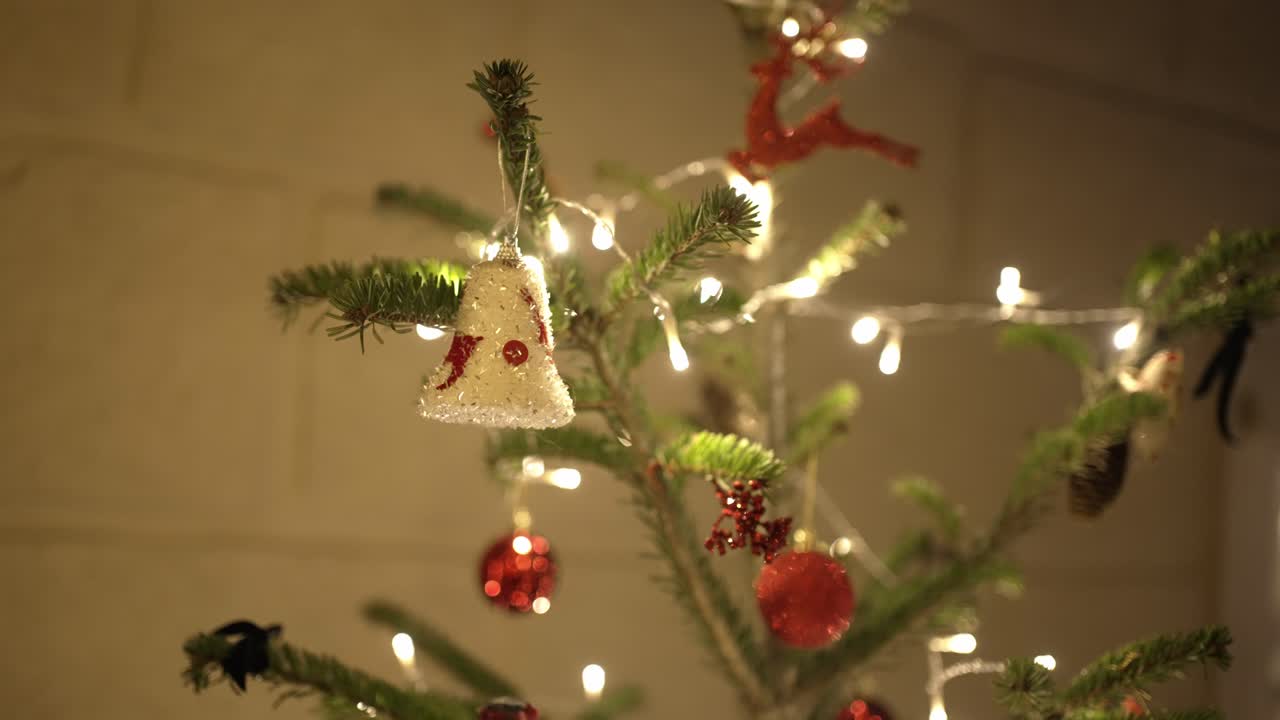 close up of sparkling bell and red ornaments hanging on a christmas tree with warm lights