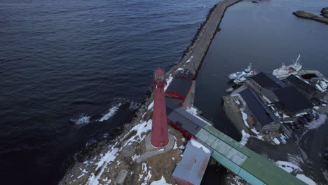 slow aerial downward panning shot of the andenes lighthouse norway, with a break wall, marina and harbor in the background