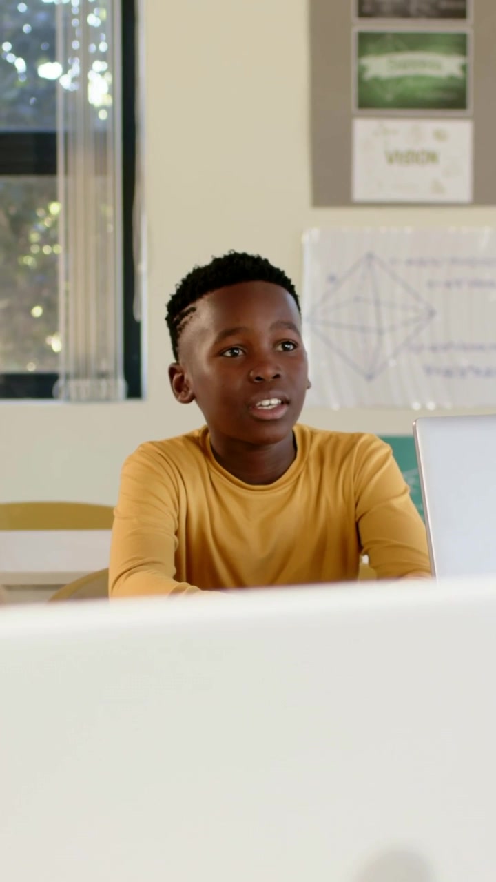 Vertical video: Responding in class youth student in mustard shirt speaking and leaning with laptop