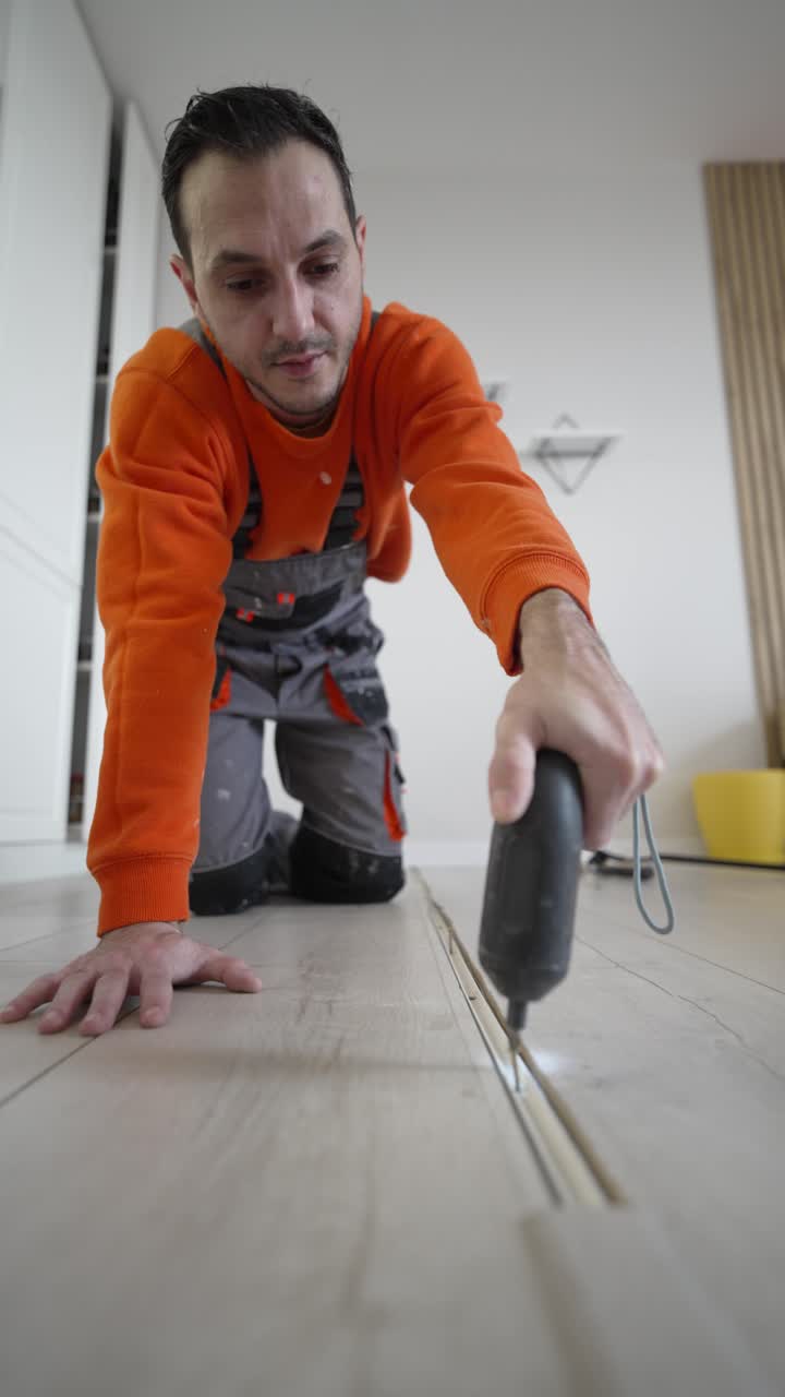 Vertical video shows a man using a electric screwdriver to fix a floor transition strip at home, capturing DIY repair, home improvement, and practical household maintenance indoors