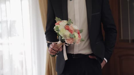 Groom-with-wedding-bouquet-in-his-hands-at-home.-White-shirt,-jacket