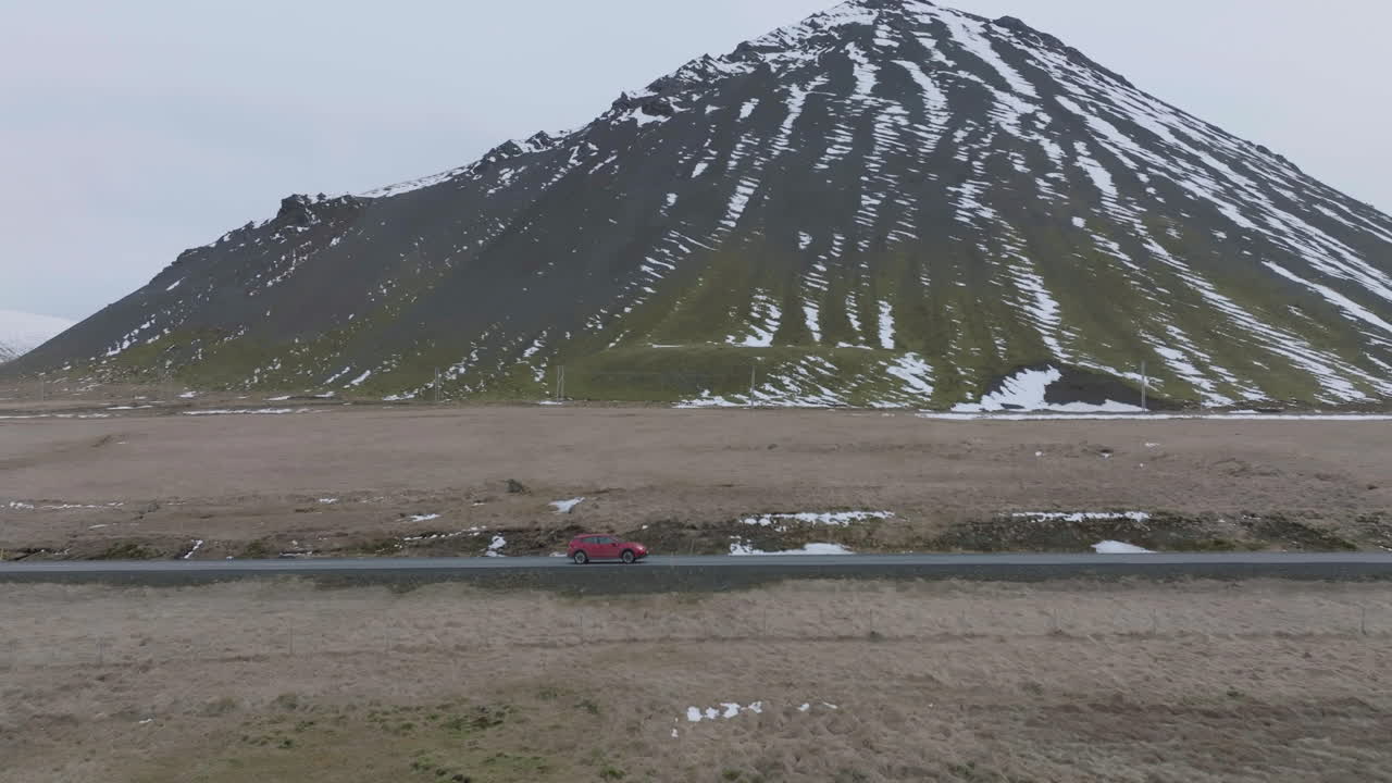 아이슬란드의 화산 언덕 옆 도로를 따라 이동하는 빨간 자동차의 드론 샷