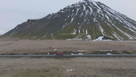 disparo de drone de un coche rojo moviéndose por una carretera junto a colinas volcánicas en el paisaje de islandia