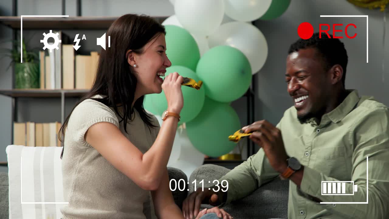 Couple exchanging gold blowers, testing and blowing on couch, celebrating with REC overlay, balloon