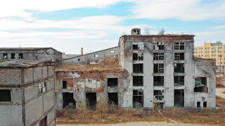 Facciata anteriore di edificio abbandonato. Vecchia fabbrica mostra la desolazione post-industriale con finestre rotte.