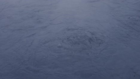 reveal shot of dark blue boiling mud pool with steam going over, iceland