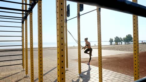workout outdoors. suspension straps. workout with straps. Athletic young woman is doing all-body resistance exercises using looped ropes TRX, at the beach during sunset or sunrise. Fitness training outdoors. healthy lifestyle concept. morning sport