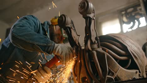 locksmith cuts and sands the decorative metal steampunk fish sculpture by electric grinder with a lot of sparks in slow motion, metalwork at workshop, 4k 60p prores hq