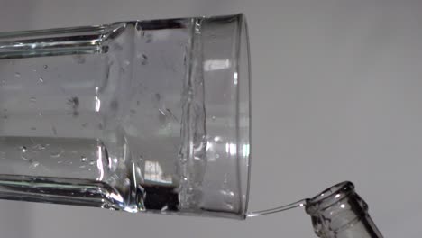 pouring water into a drinking glass on a grey studio background - vertical