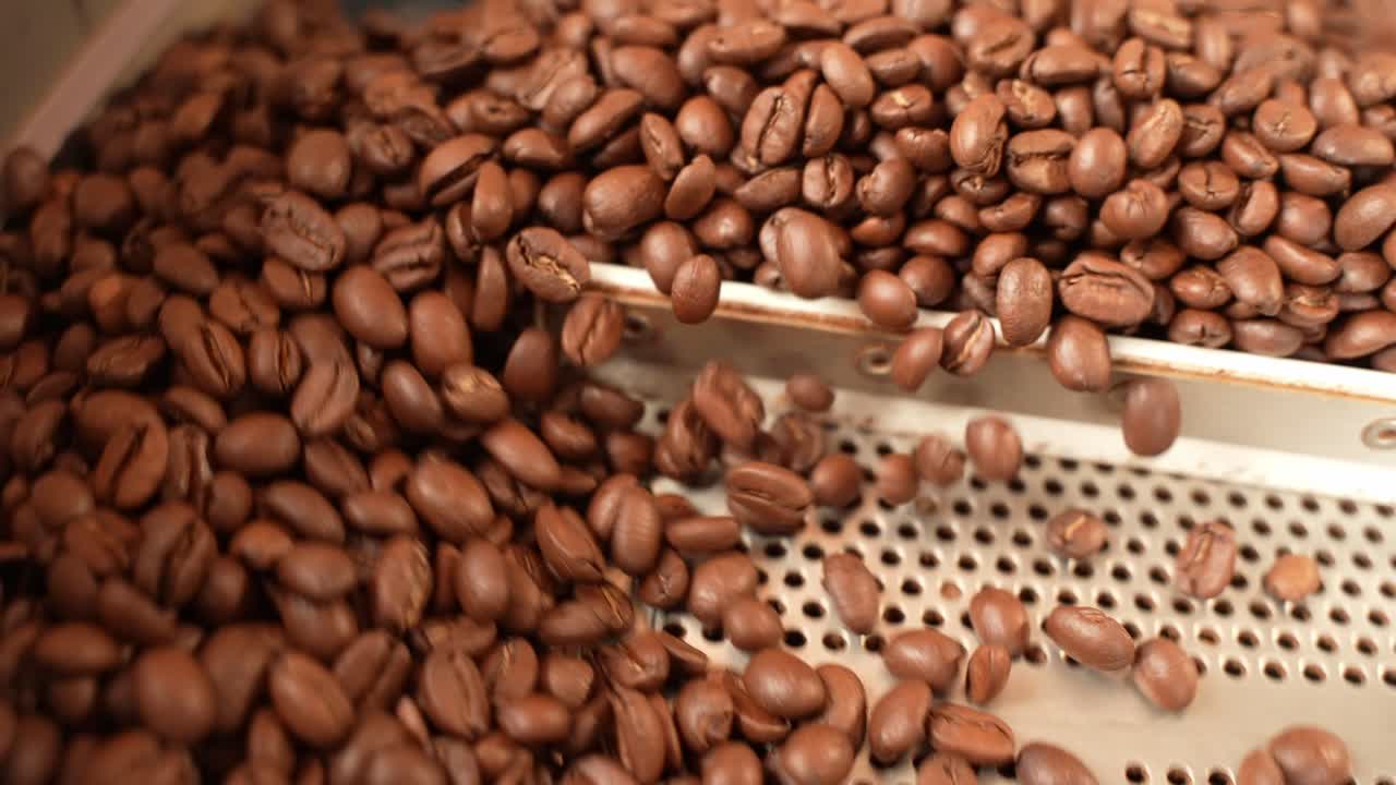Chicchi di caffè aromatici appena tostati spinti fuori da una macchina tostatrice - primo piano al rallentatore.