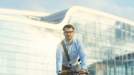 Handsome-man-in-business-style-riding-a-bicycle-and-stopping-in-front-of-the-camera