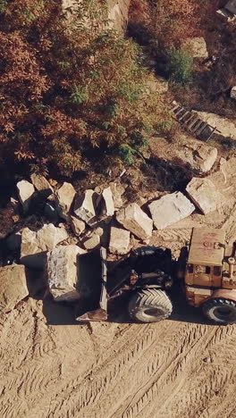 yellow bulldozer with a bucket is carrying a large stone near a sand quarry. camera motion down. close-up. vertical video