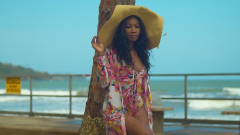 sexy african girl in a bikini stands at a coconut tree with waves from the ocean in the background