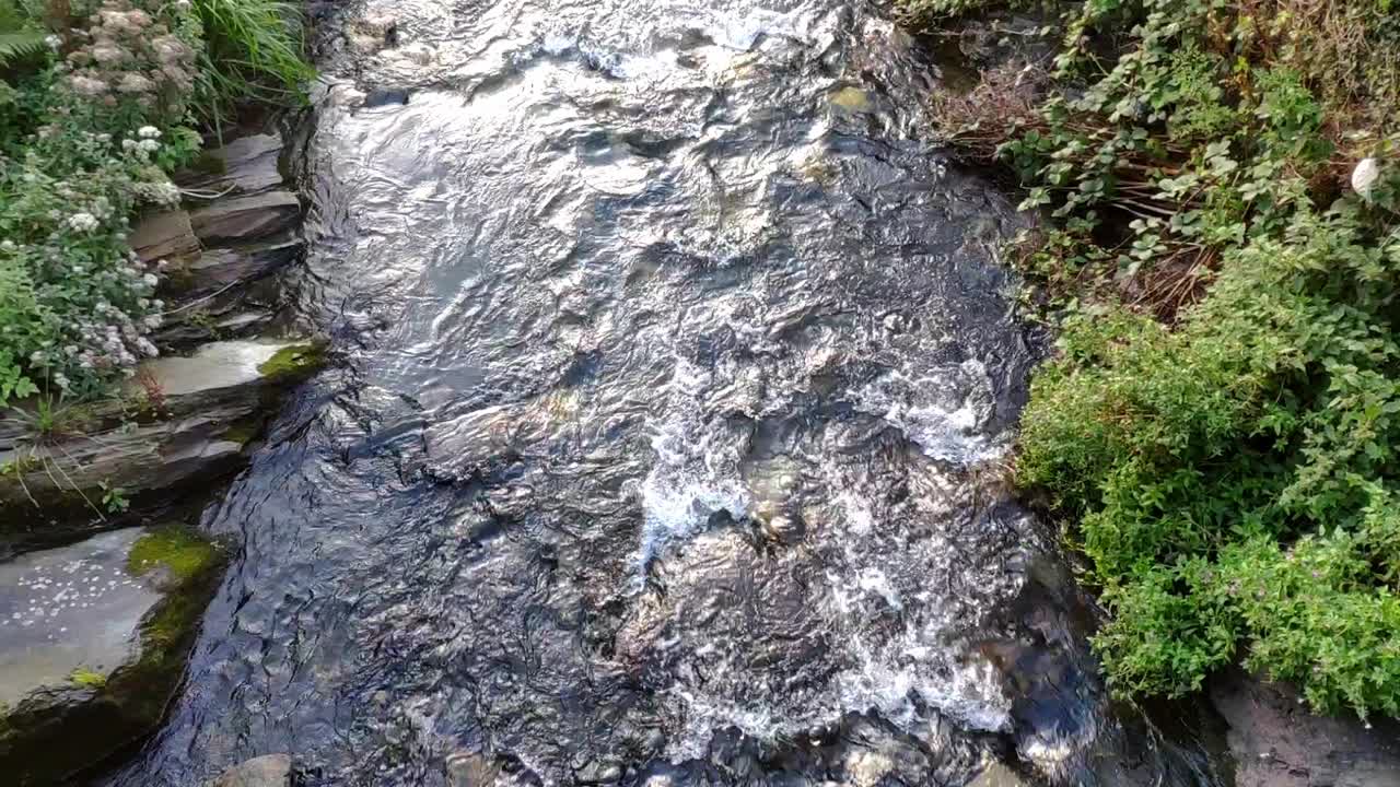 River in Boscastle village , Cornwall (England).Stream of water flowing. Shallow water and rocks are seen below. Lime stone on the sides. Some sunlight from sunset.