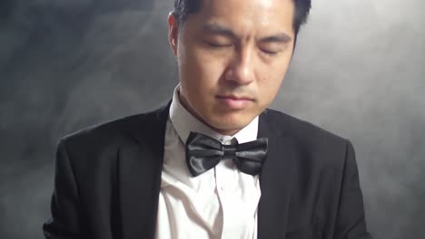 close up of asian conductor man holding a baton closing his eyes and showing gesture in the black studio with fog