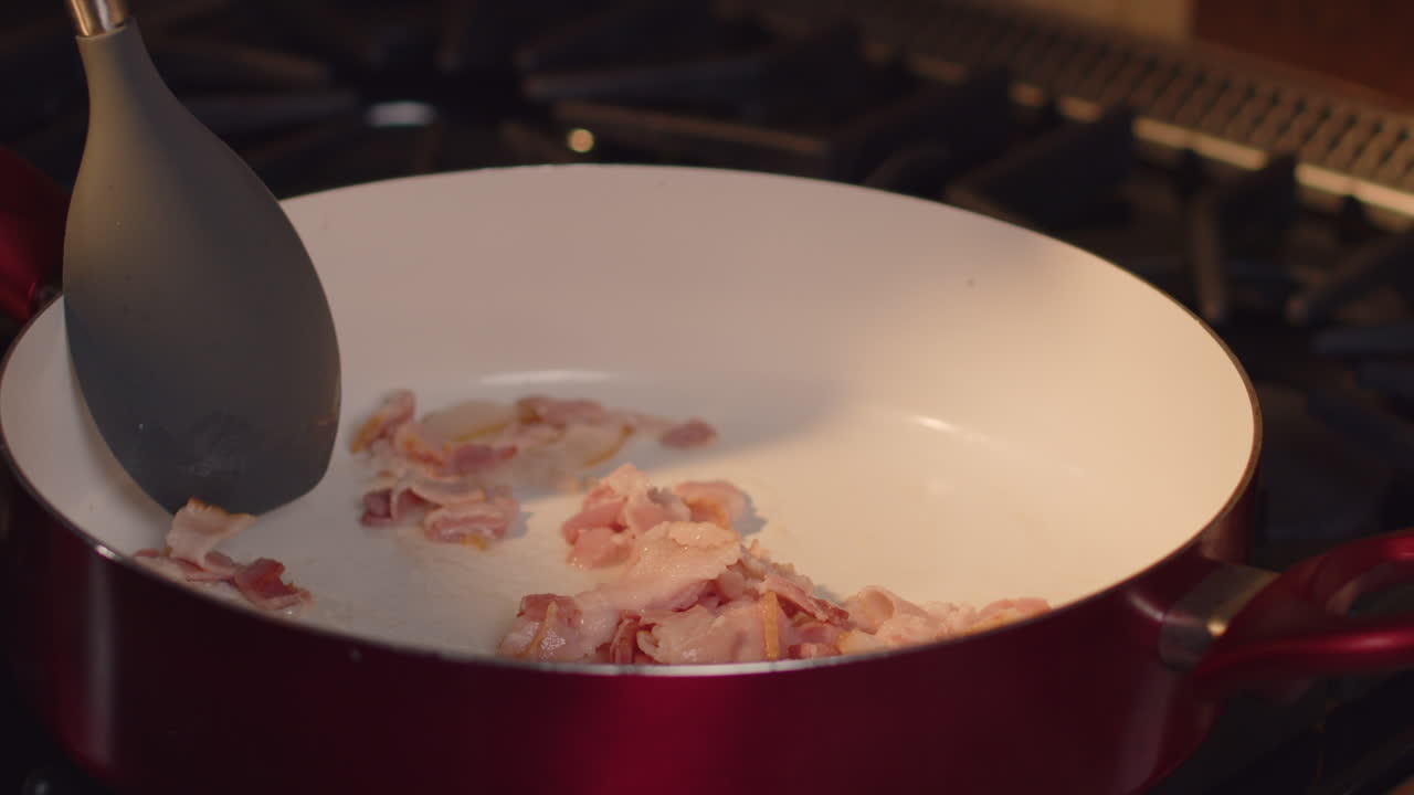 Chopped bacon being stirred with a spoon and fat rendered in to hot pan