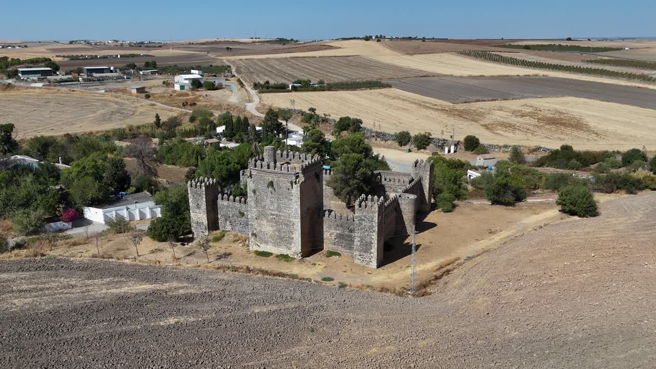 Aerial orbit around Castillo de las Aguzaderas, Castle near El Coronil, Seville, Spain, revealing its preserved stone walls and towers surrounded by a dry, sunlit Andalusian landscape