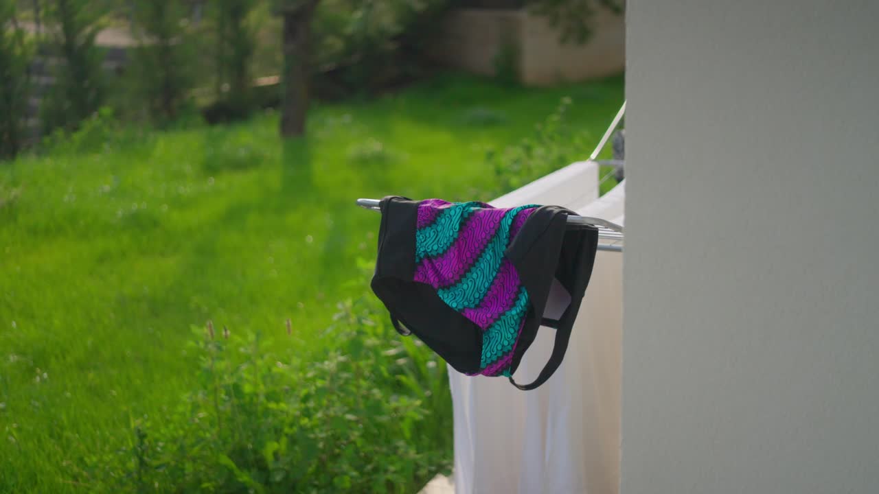 Costume da bagno colorato che asciuga su uno stendibiancheria in un giardino verde.