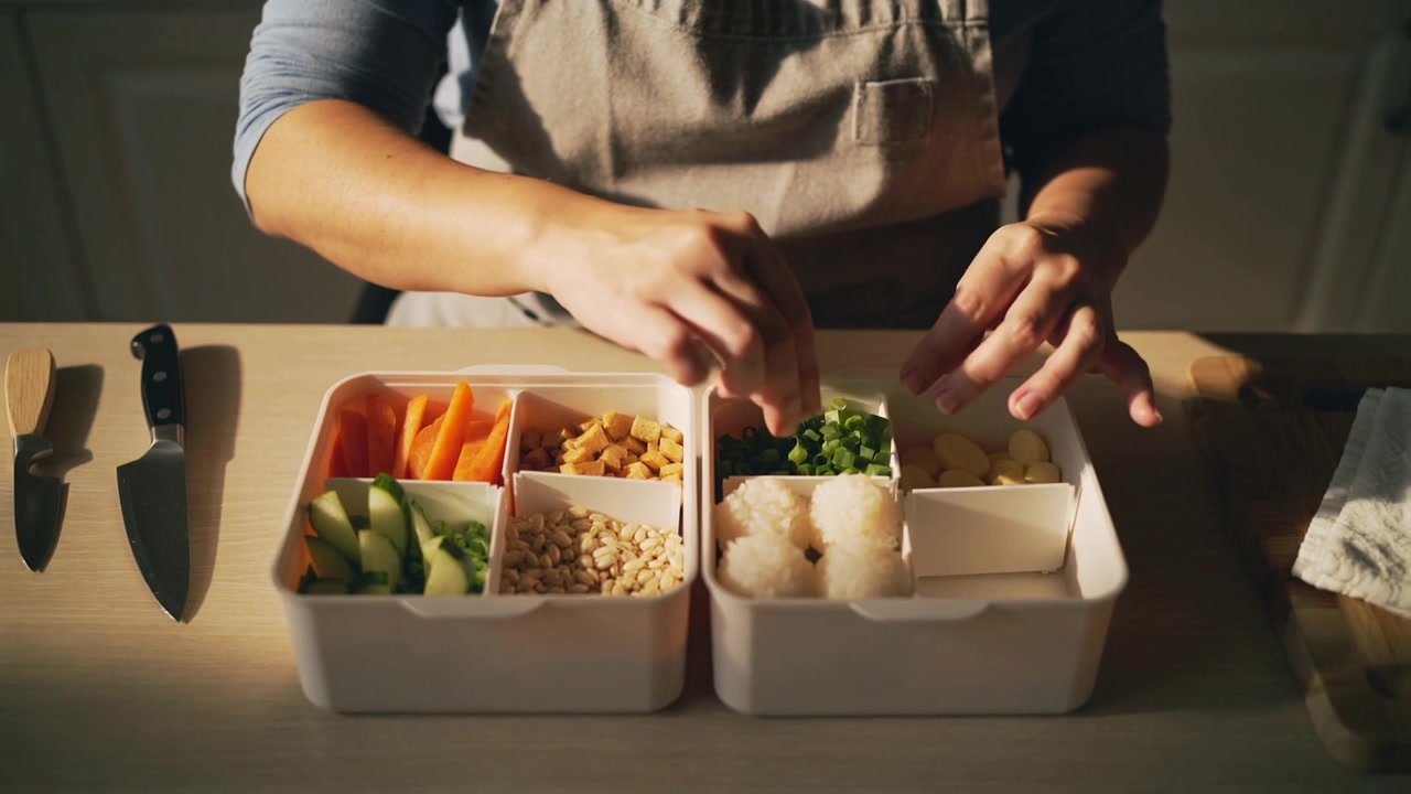 Picking up herbs aproned cook packing greens riceballs into bento in kitchen finishing taking cloth
