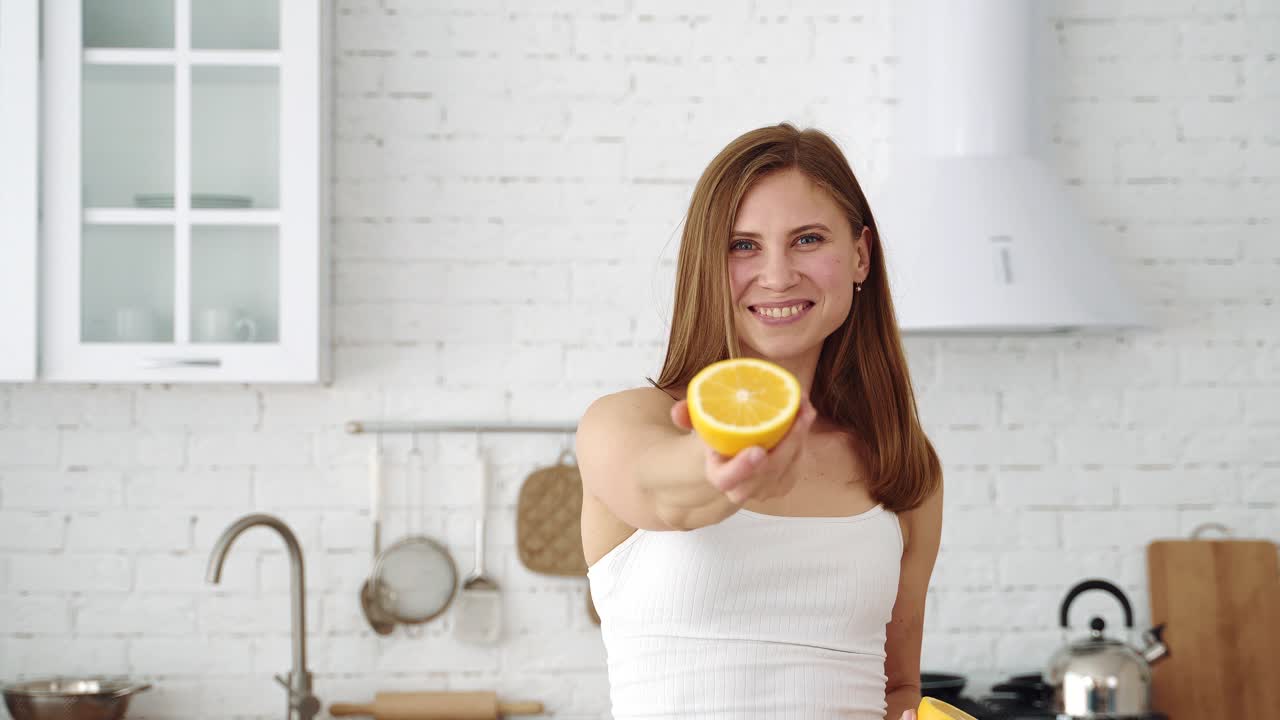 A smiling girl in the kitchen offers an orange slice in her hand