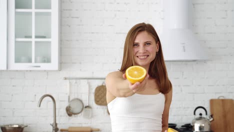 a smiling girl in the kitchen offers an orange slice in her hand