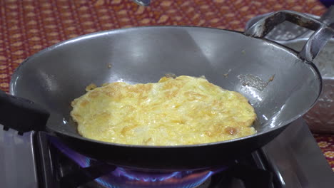 vista de cerca de una tortilla que se cocina en un wok de acero en una estufa de butano