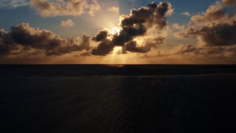 beautiful aerial left trucking drone shot of an ocean sunrise at well beach near joao pessoa on a warm summer morning with the water below, golden clouds on the skyline, and small boats in the water