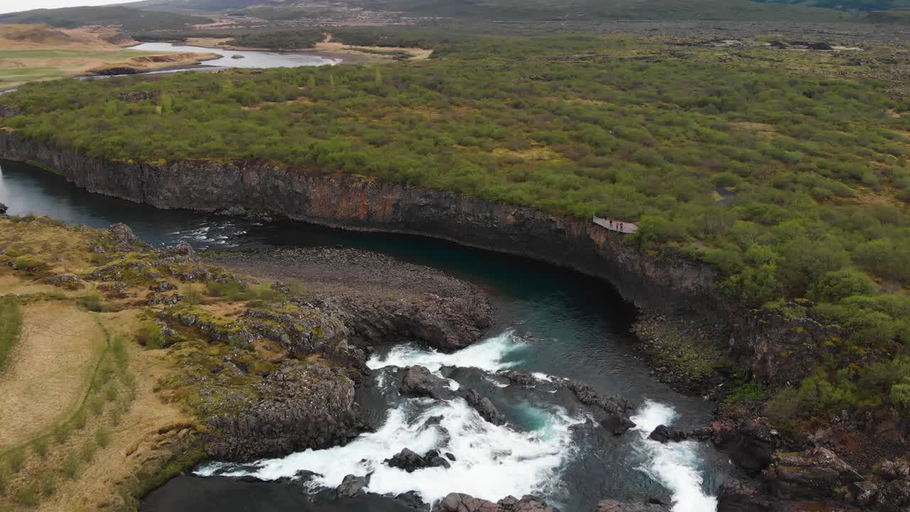 The less crowded but beautiful waterfall Glanni seen from above, surrounded by a magical Icelandic landscape with lush green bushes and majestic mountains in the background