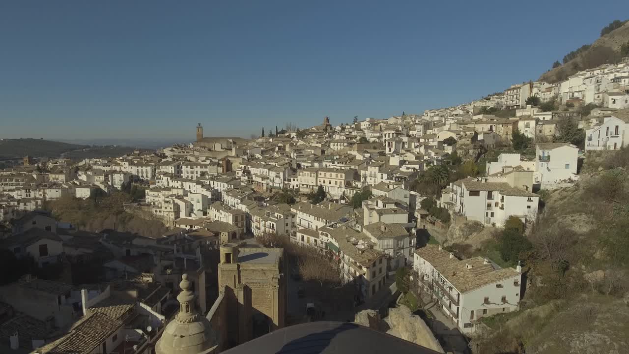 disparo de un dron que revela desde detrás del muro restante de la iglesia católica renacentista de santa maría, revelando casas blancas en cazorla, jaén, andalucía, españa