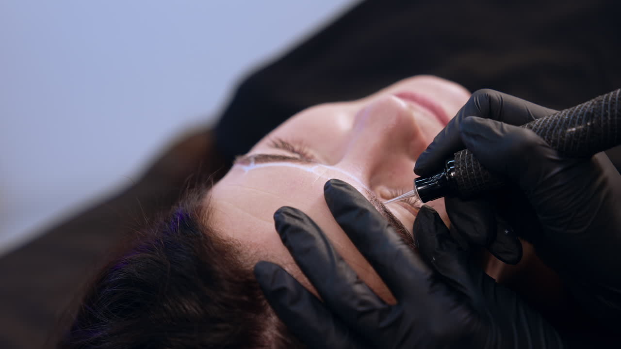 Beautician uses a special device to apply permanent make up on client's eyebrows. Salon beauty procedure. Close up.