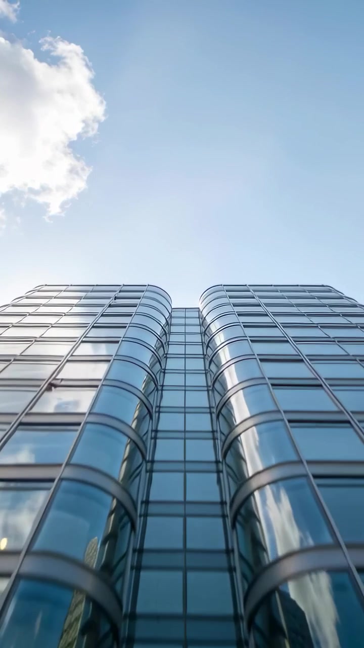 Video vertical: Cámara alejándose de la calle, revelando dos torres gemelas de cristal curvado que reflejan el cielo.